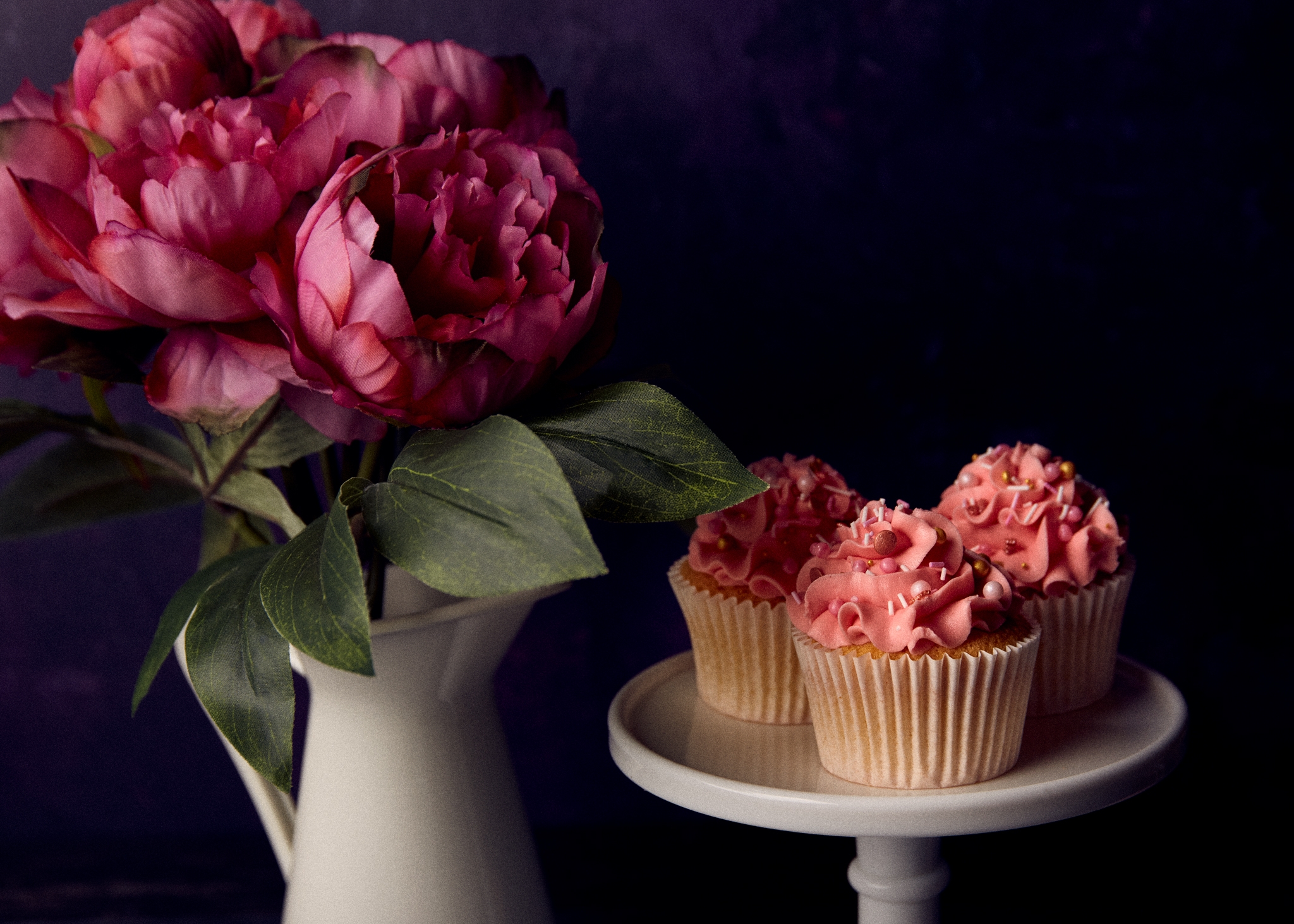 perfect product photos, cupcakes with pink frosting placed on a table alongside a vase full of pink roses