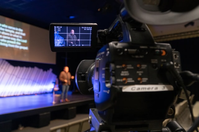 Investing in Event Photography Services can have a positive impact on your event; a photographer capturing a picture of people on stage